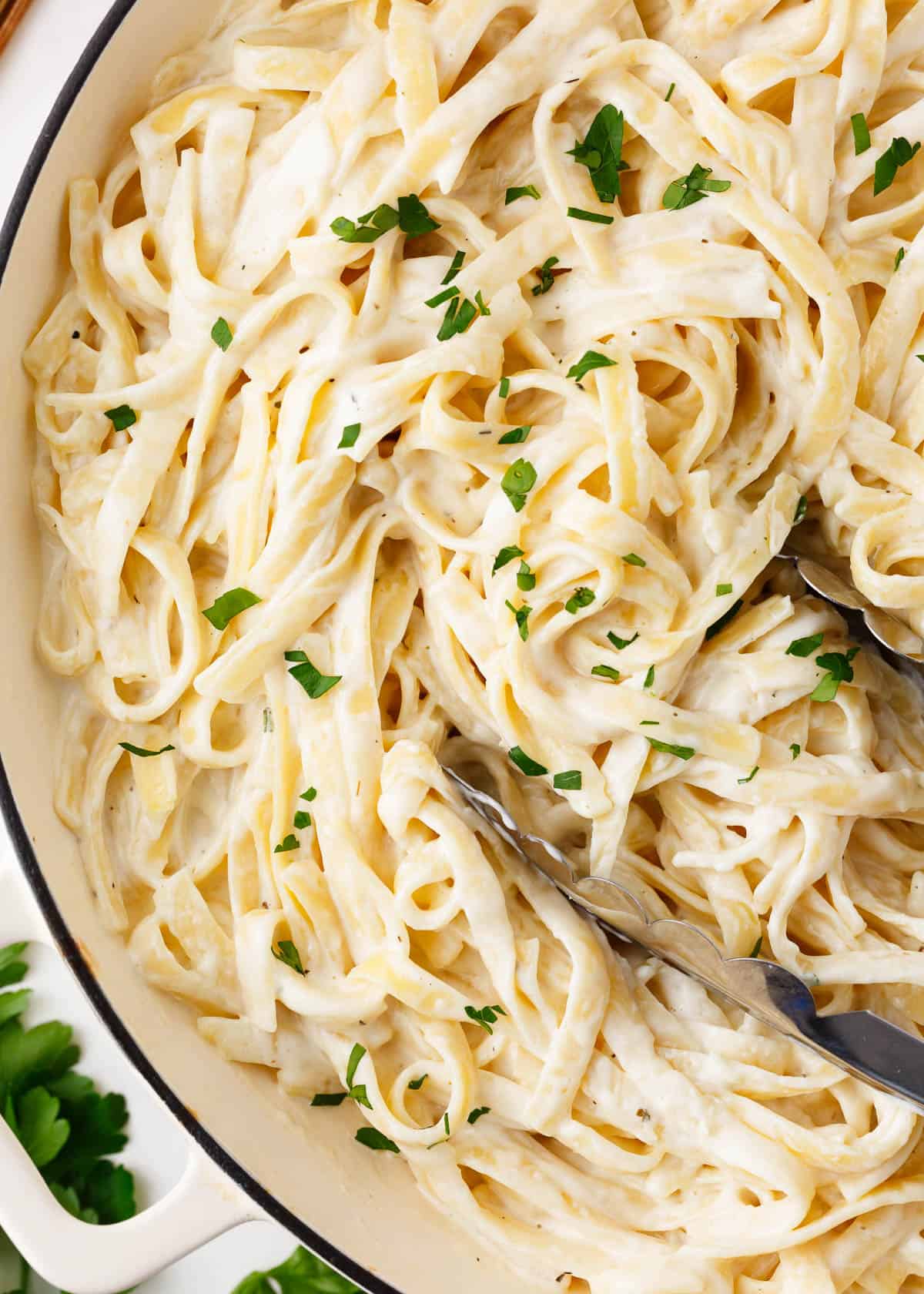 Homemade alfredo sauce in a white pot garnished with parsley.