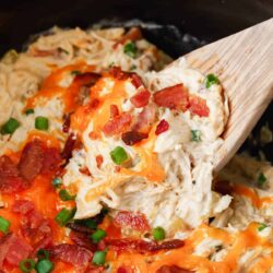 Crockpot crack chicken being served from the slow cooker with a wooden spoon.