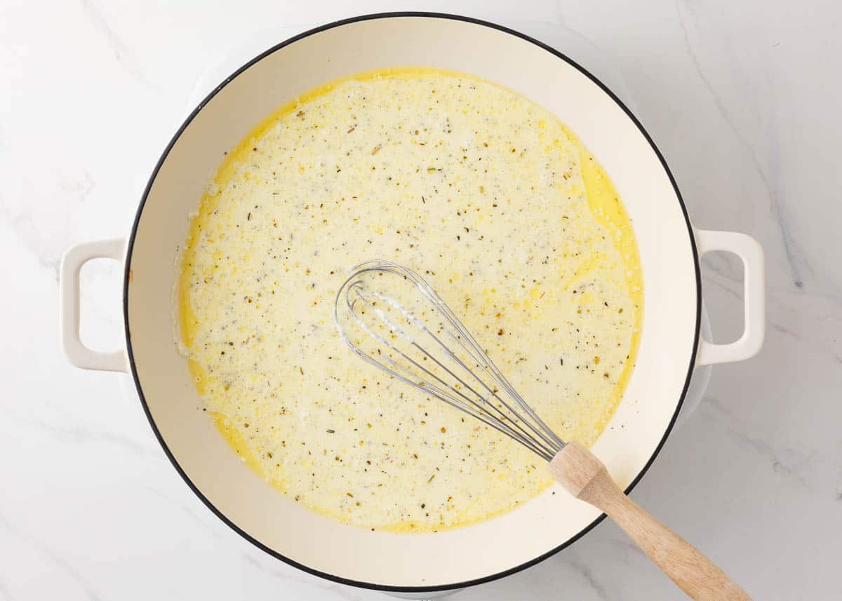 Making alfredo sauce in a white pot with butter, garlic, cream cheese, heavy cream and garlic.