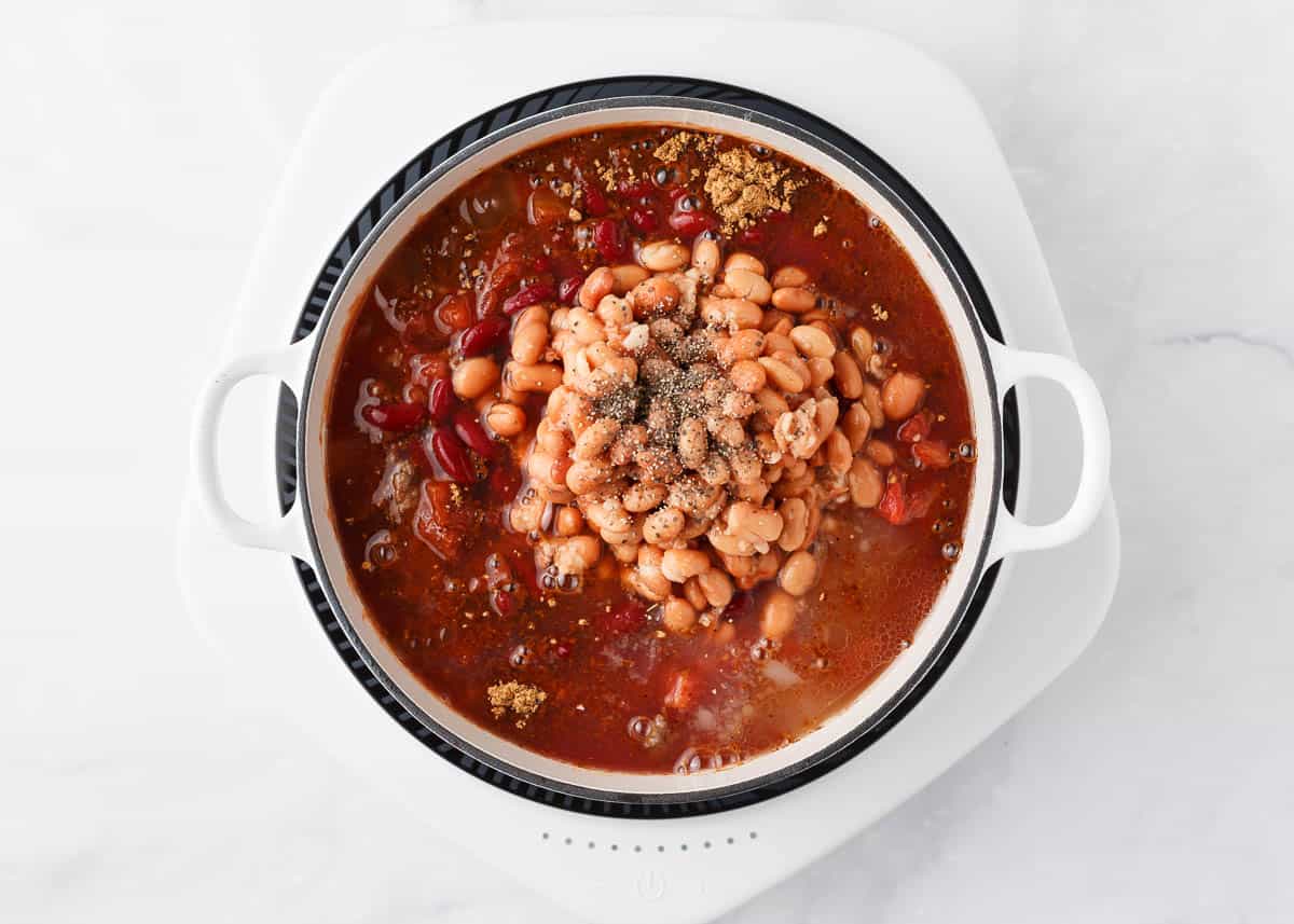 Beans, seasonings and tomatoes added to a pot.