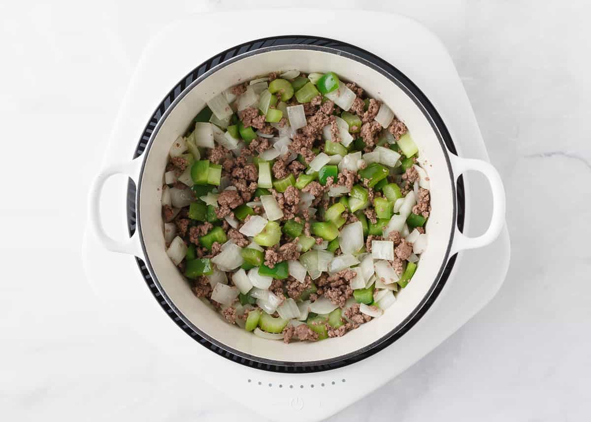 Ground beef, onion and peppers in a white pot.