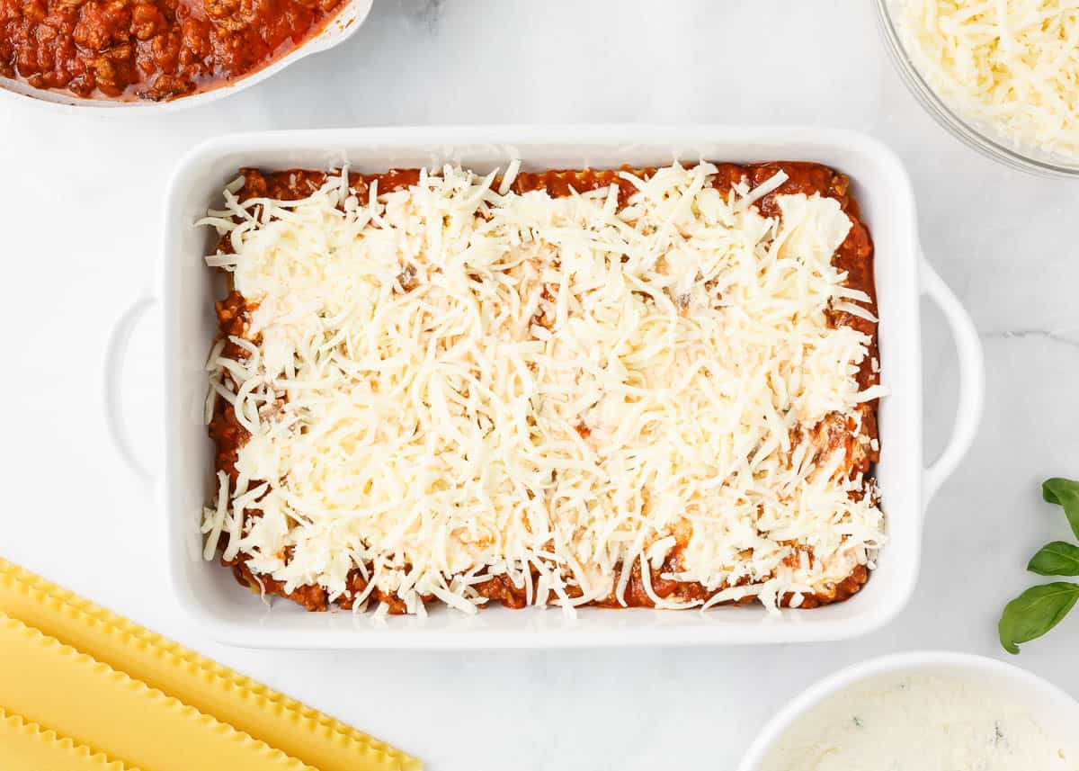 Cheese over a layer of ricotta, meat sauce and noodles in a baking dish. 