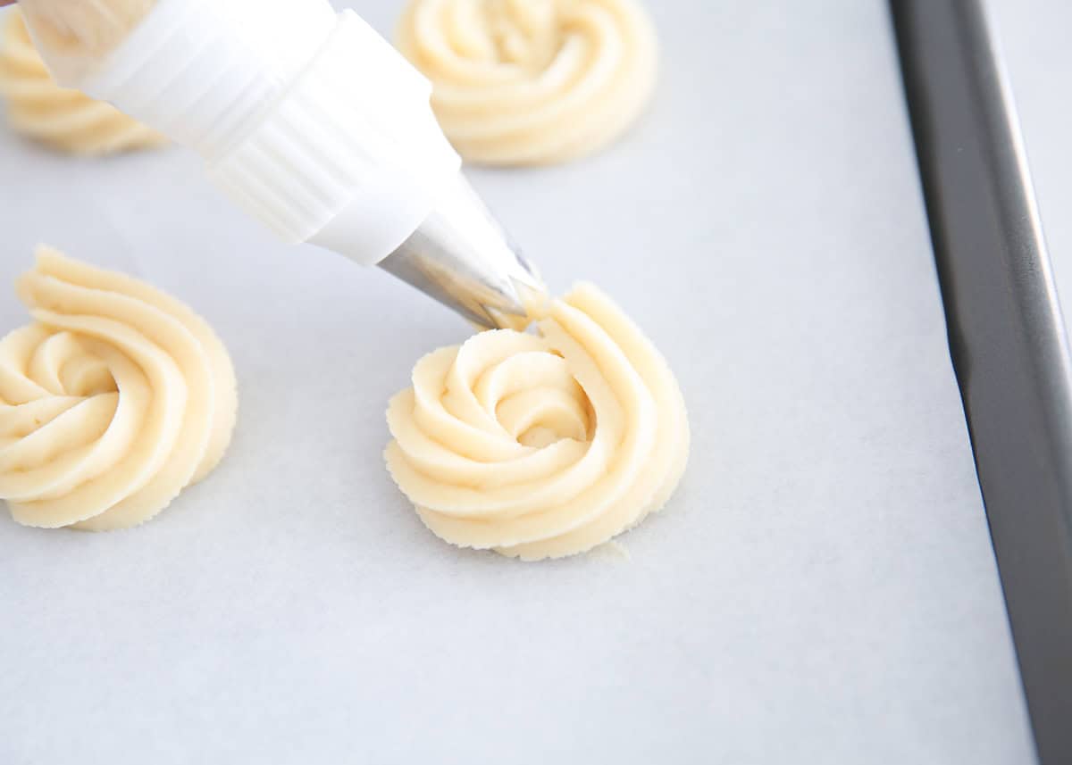 Piping butter cookies onto parchment lined baking pan.