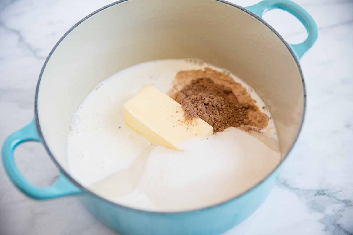 Butter, sugar, milk and cocoa powder in a blue pot.