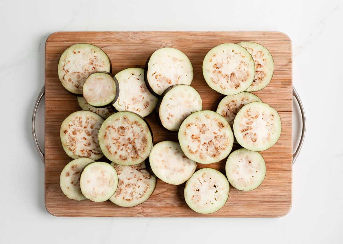 Salted slices of eggplant sweating on a cutting board.