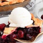 A piece of cherry pie with a scoop of ice cream on a plate.