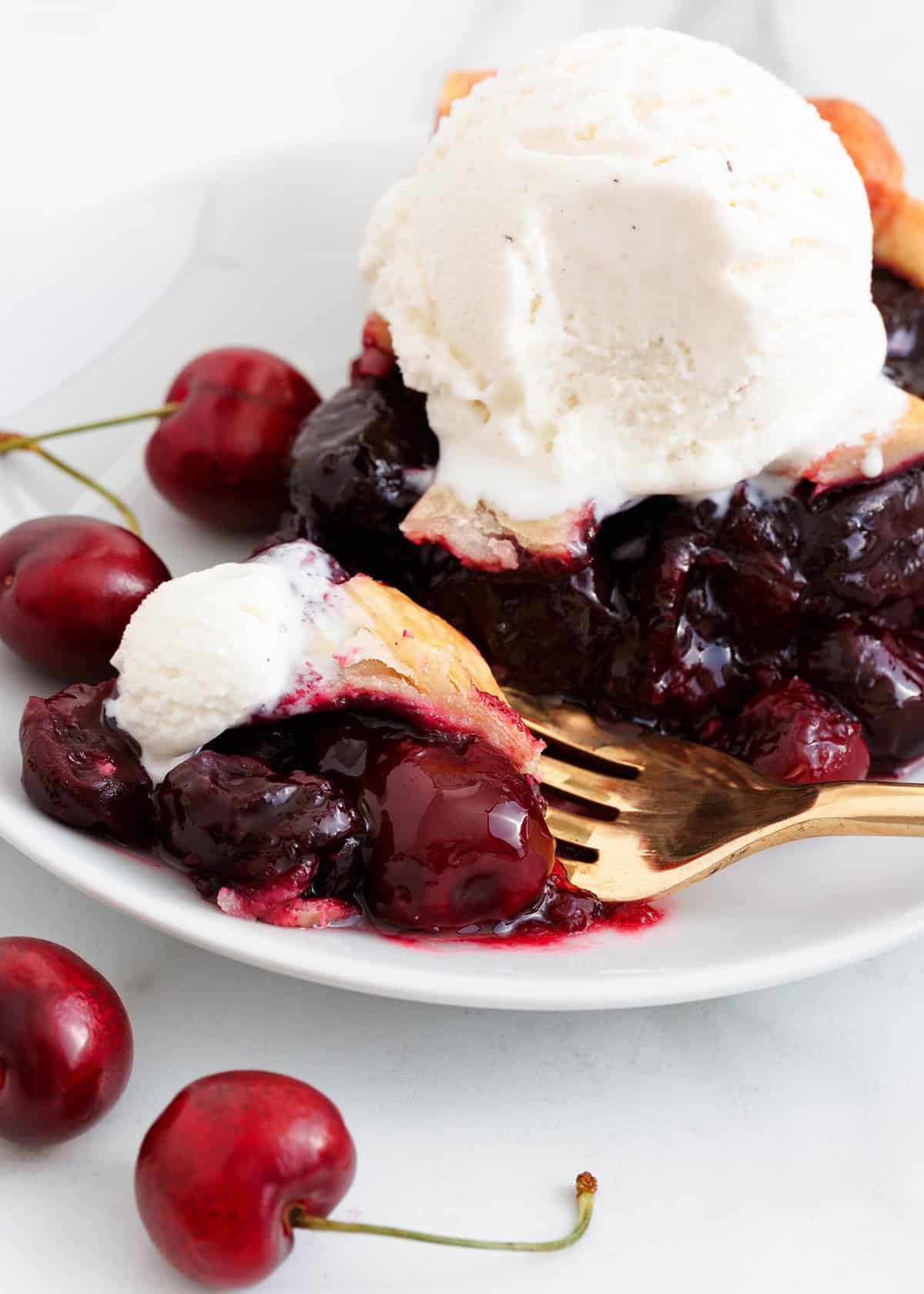 A slice of pie with cherry pie filling on a plate with a scoop of ice cream.