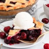 A slice of cherry pie on a plate with ice cream and a fork.