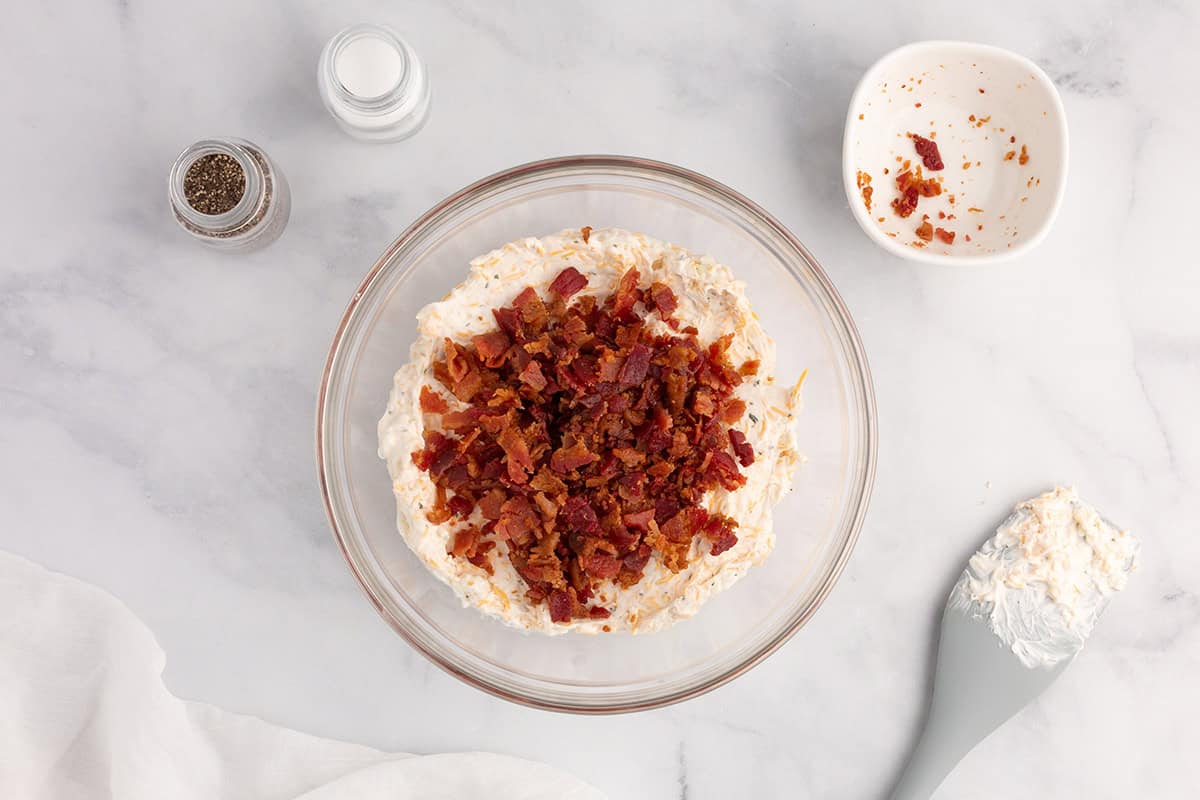 Bacon being added to dip in a bowl.