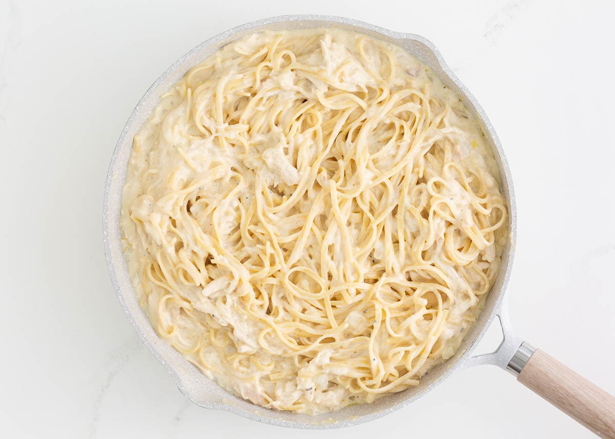 Noodles tossed with creamy sauce in a skillet.