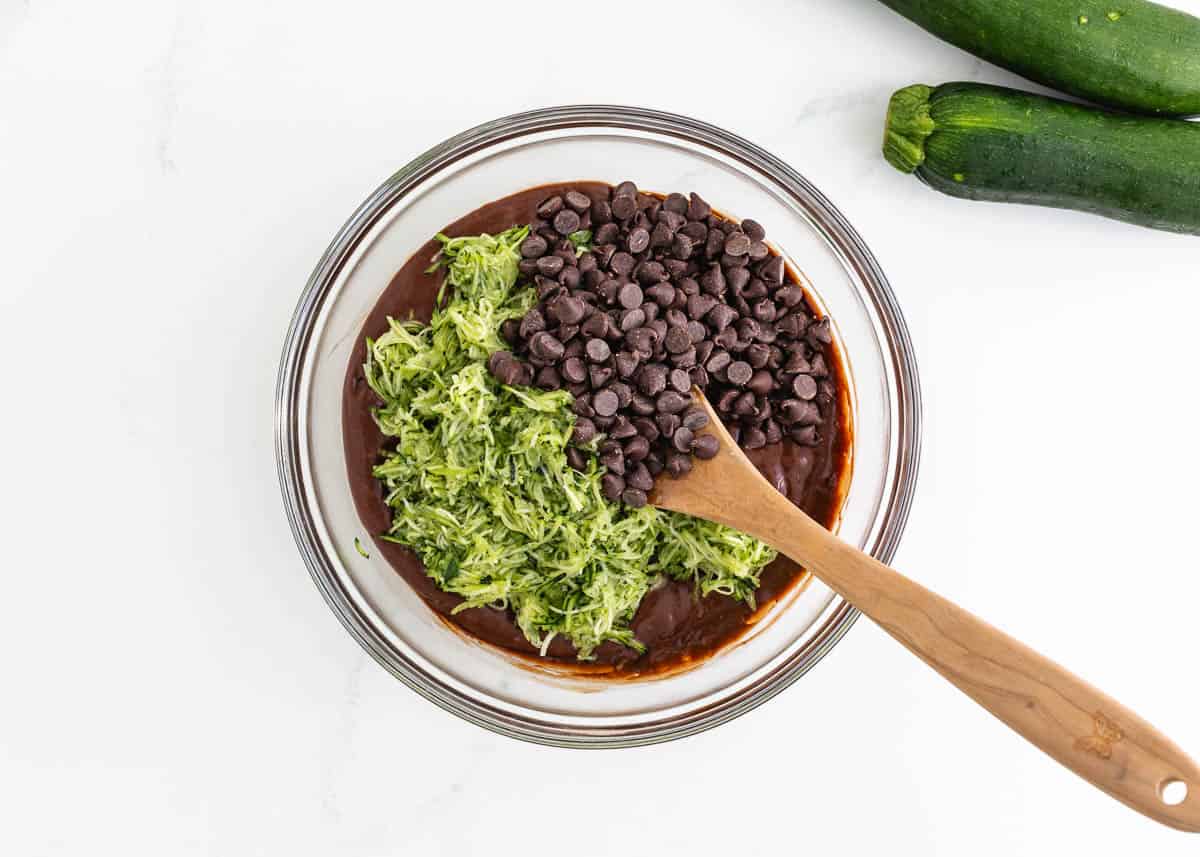 Adding shredded zucchini and chocolate chip to a bowl of quick bread batter.