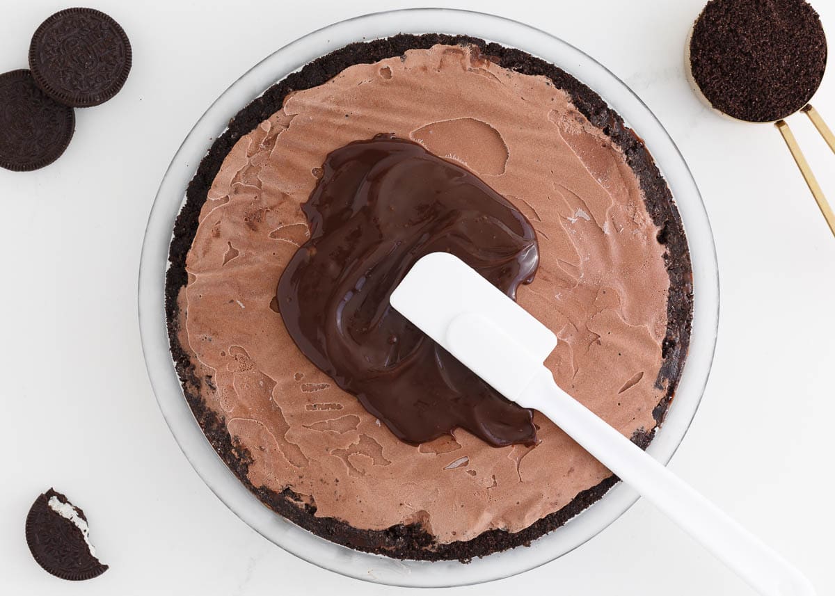 Spreading hot fudge on top of ice cream in an Oreo crust.