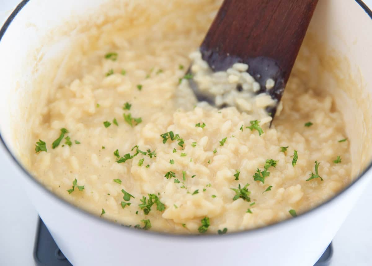 Risotto with Parmesan and herbs being stirred in a white pot.