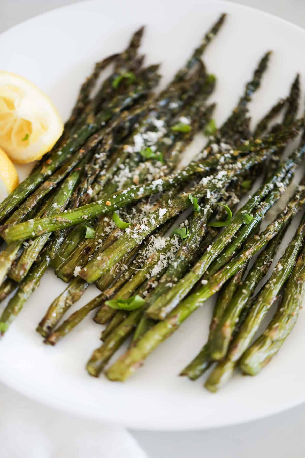 Grilled asparagus on a white plate with lemon slices.