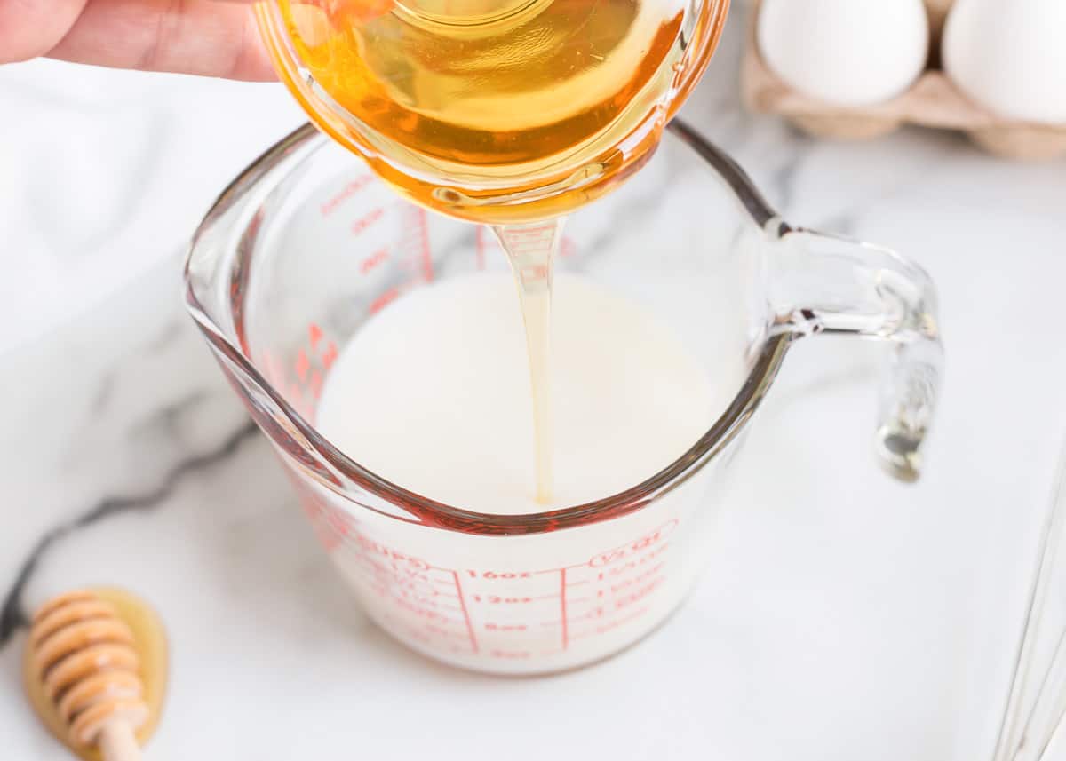 Honey being poured into milk in a measuring cup.