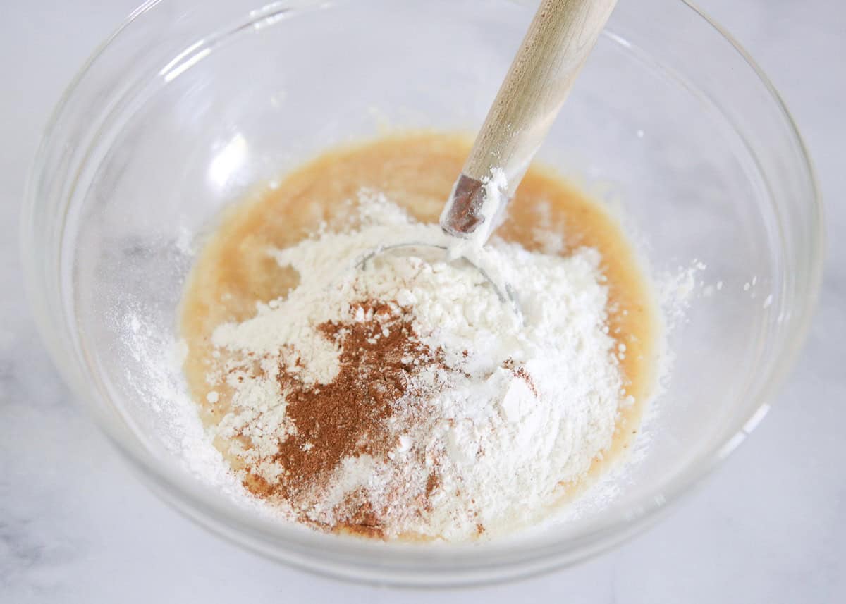 Adding flour, cinnamon and baking staples to a bowl with applesauce and mashed banana.