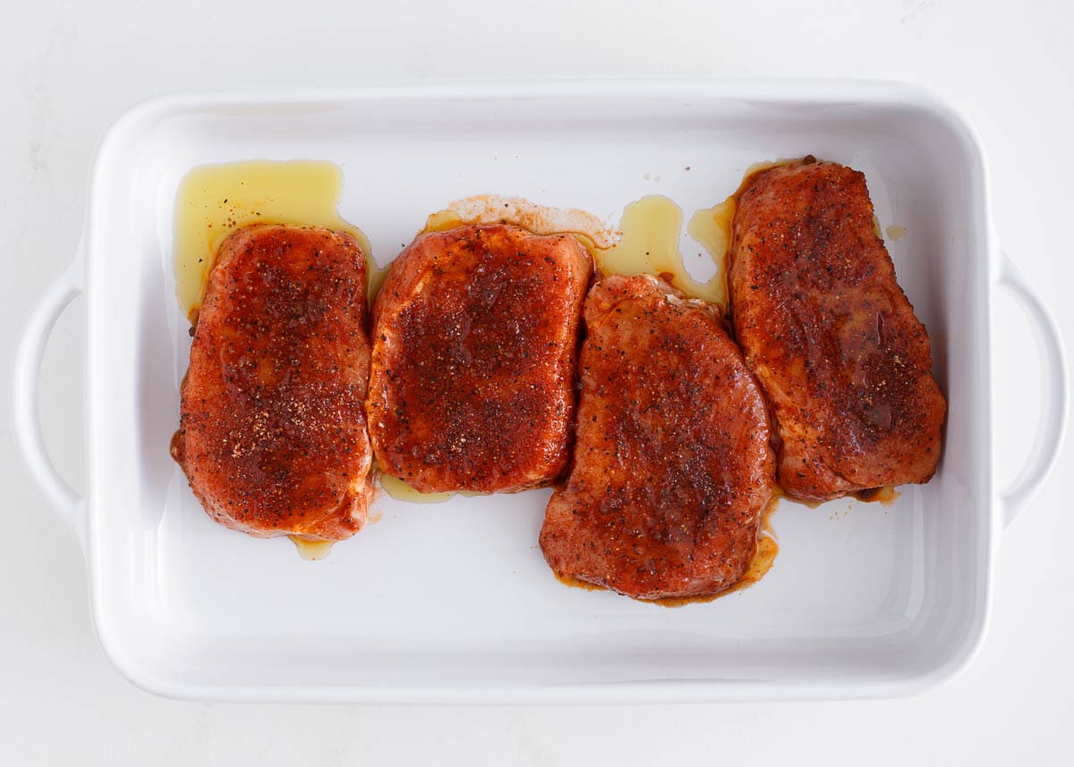 Seasoned pork chops in a white dish.