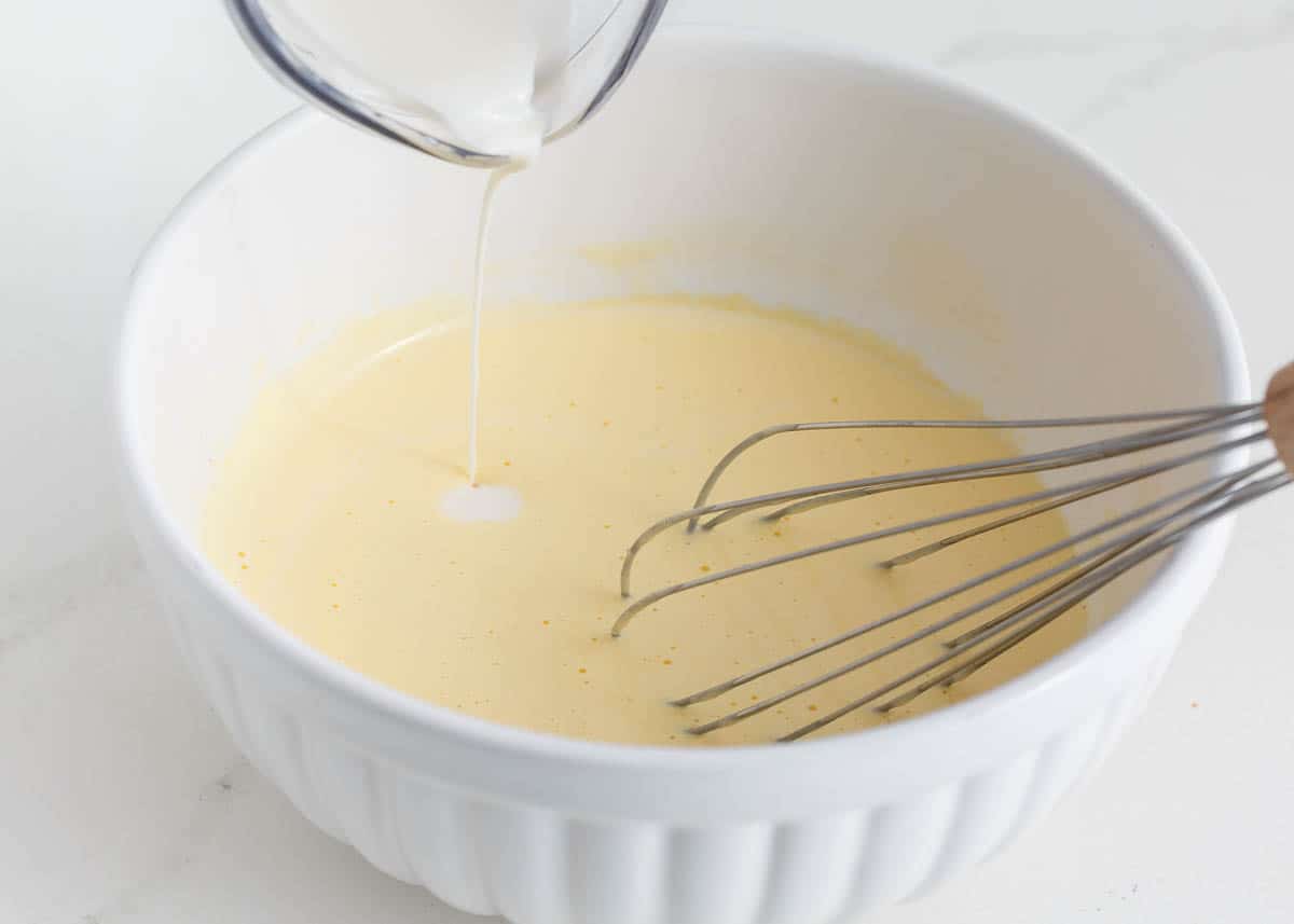 Beating eggs in a bowl and adding cream.