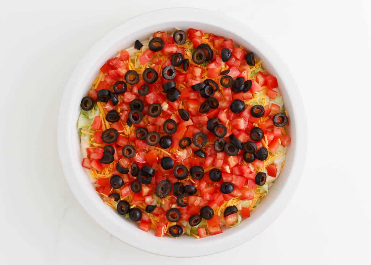 Cream cheese taco dip layered with tomatoes, lettuce and olives.