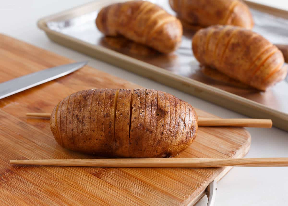 Two chopsticks on either side of a potato showing how to cut into thin slices.