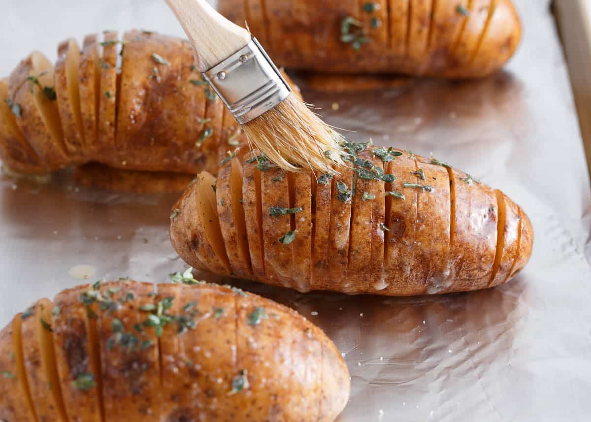 Brushing thinly sliced potatoes with butter and herbs.