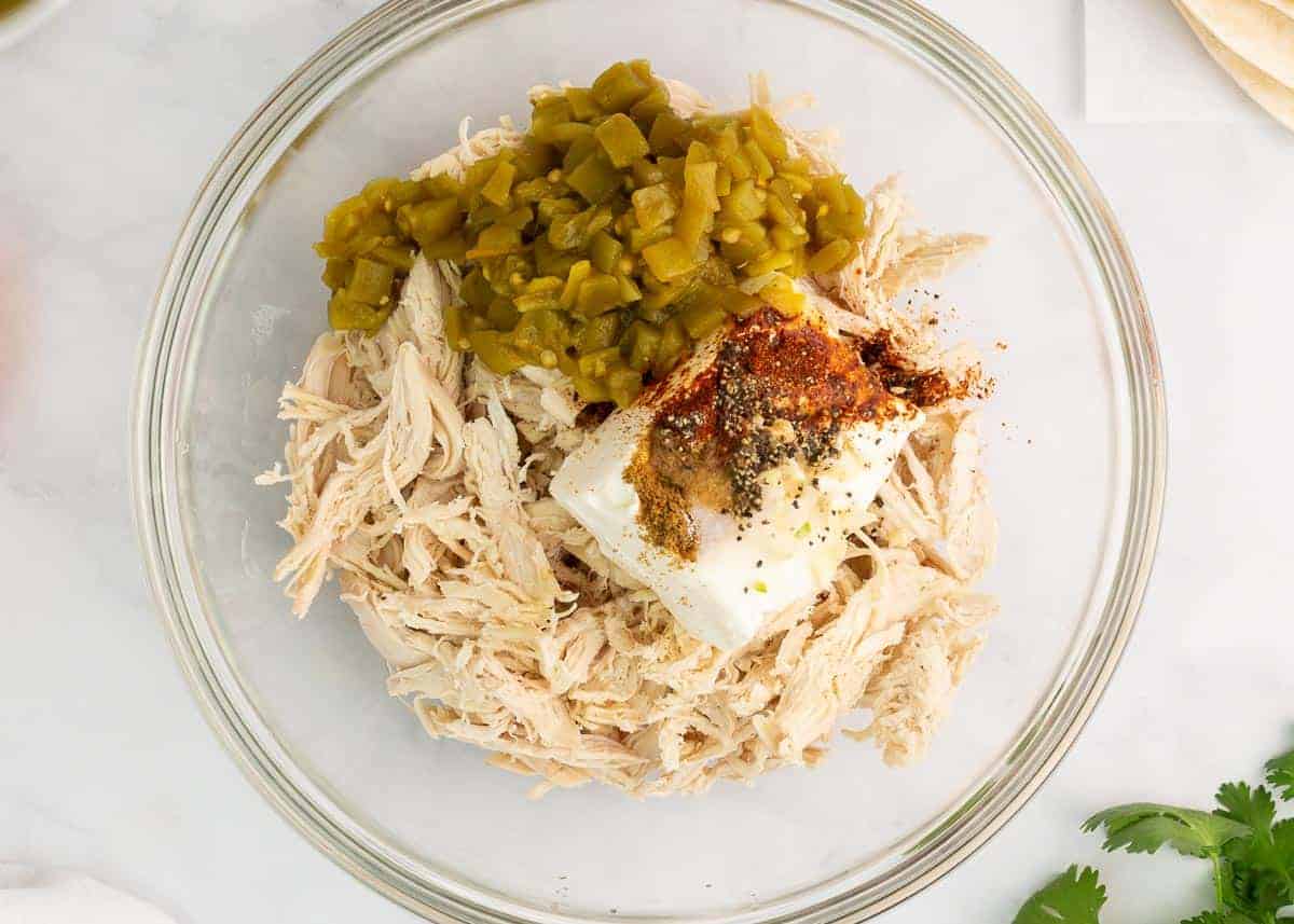 Chicken, green chiles, cream cheese and spices in a bowl.