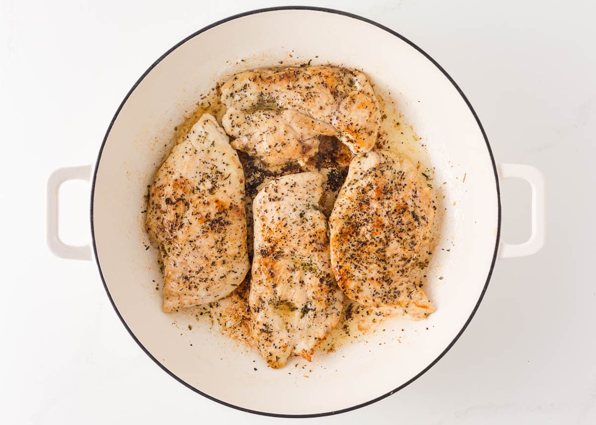 Chicken breasts with seasonings in a large skillet.