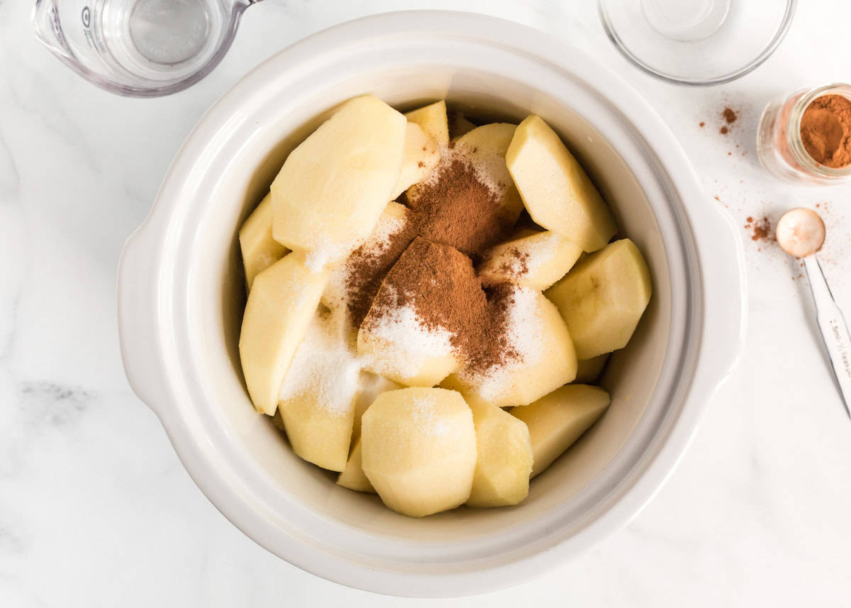 Peeled and quartered apples in crockpot with cinnamon, sugar and lemon juice.