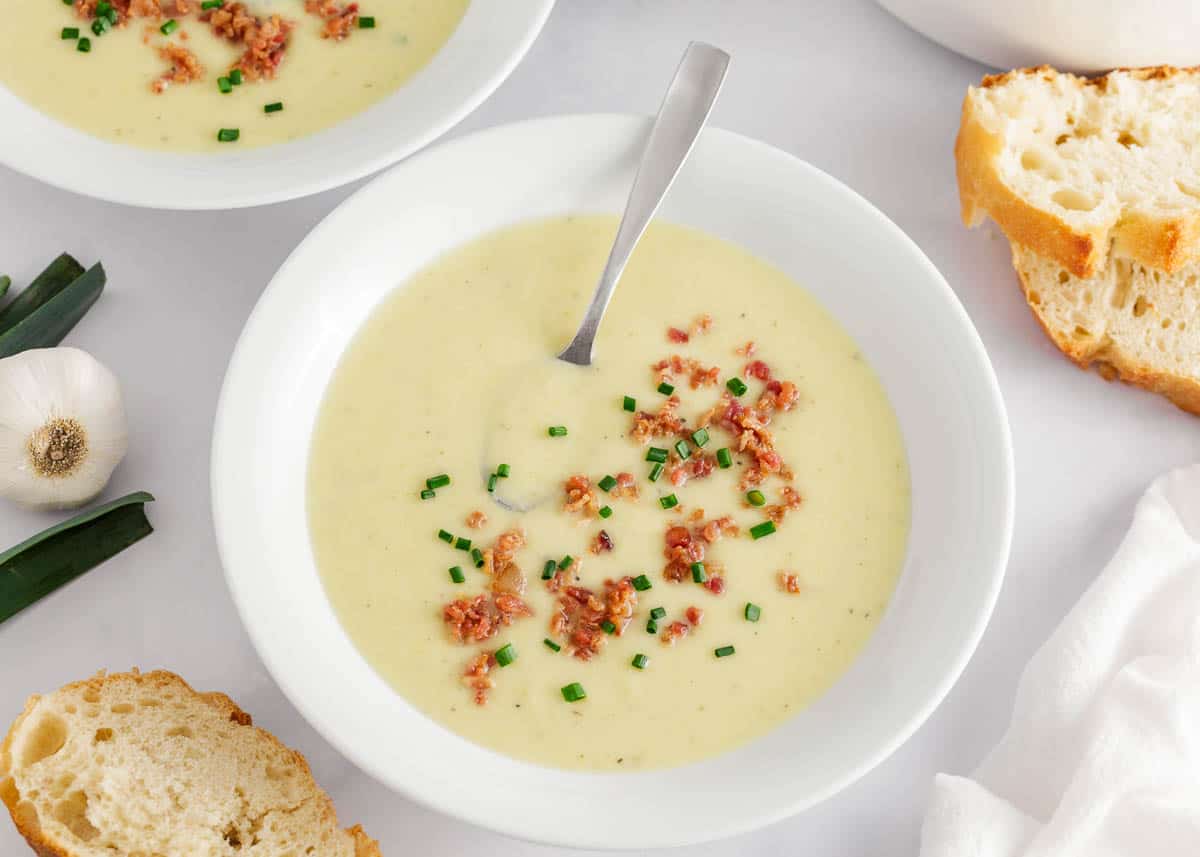 Potato leek soup in a bowl with spoon and bread on the table.