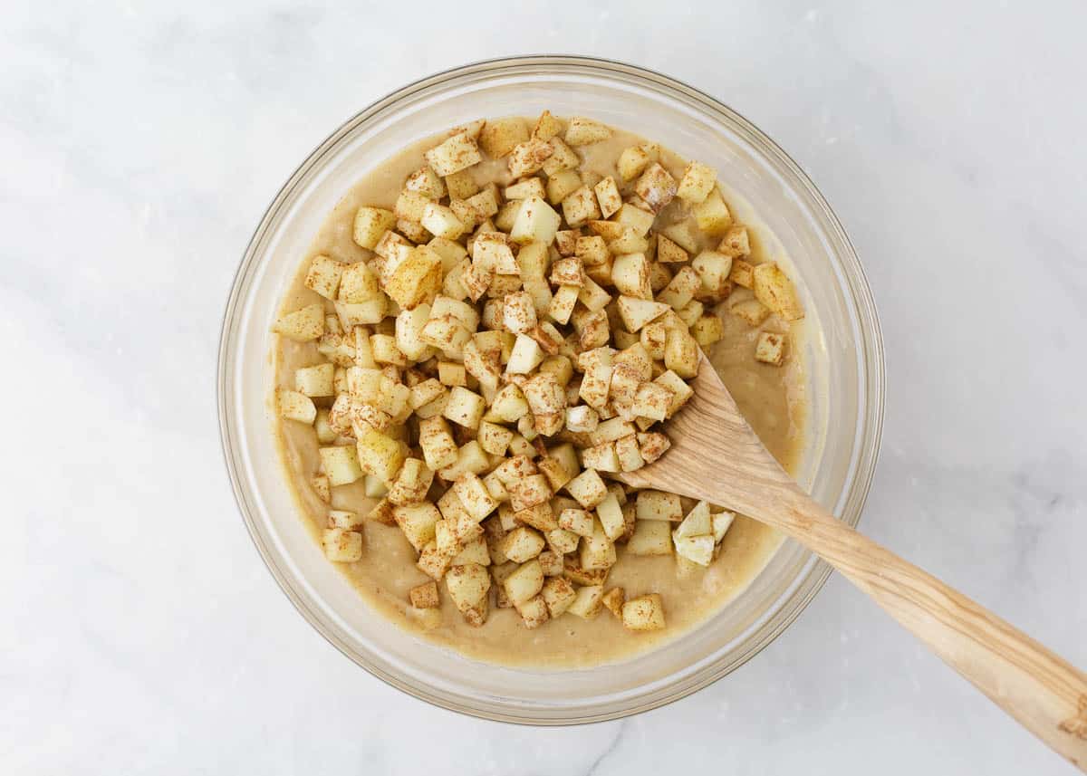 Diced apples being mixed into a muffin batter in a bowl.