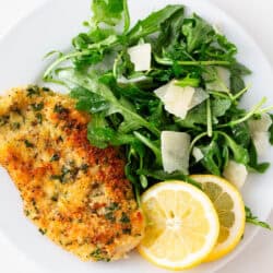 Chicken milanese with arugula salad on a plate with lemon slices.