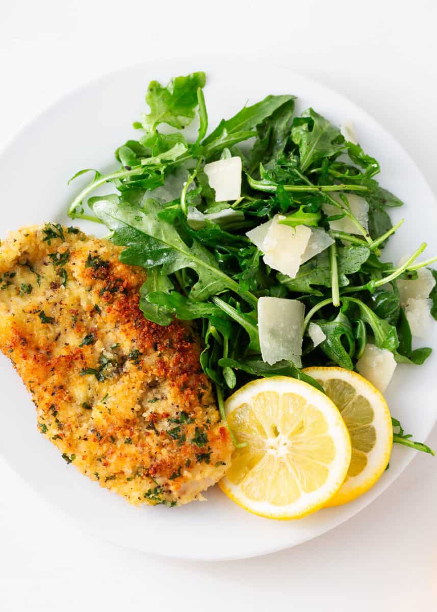 Chicken milanese with arugula salad on a plate with lemon slices.