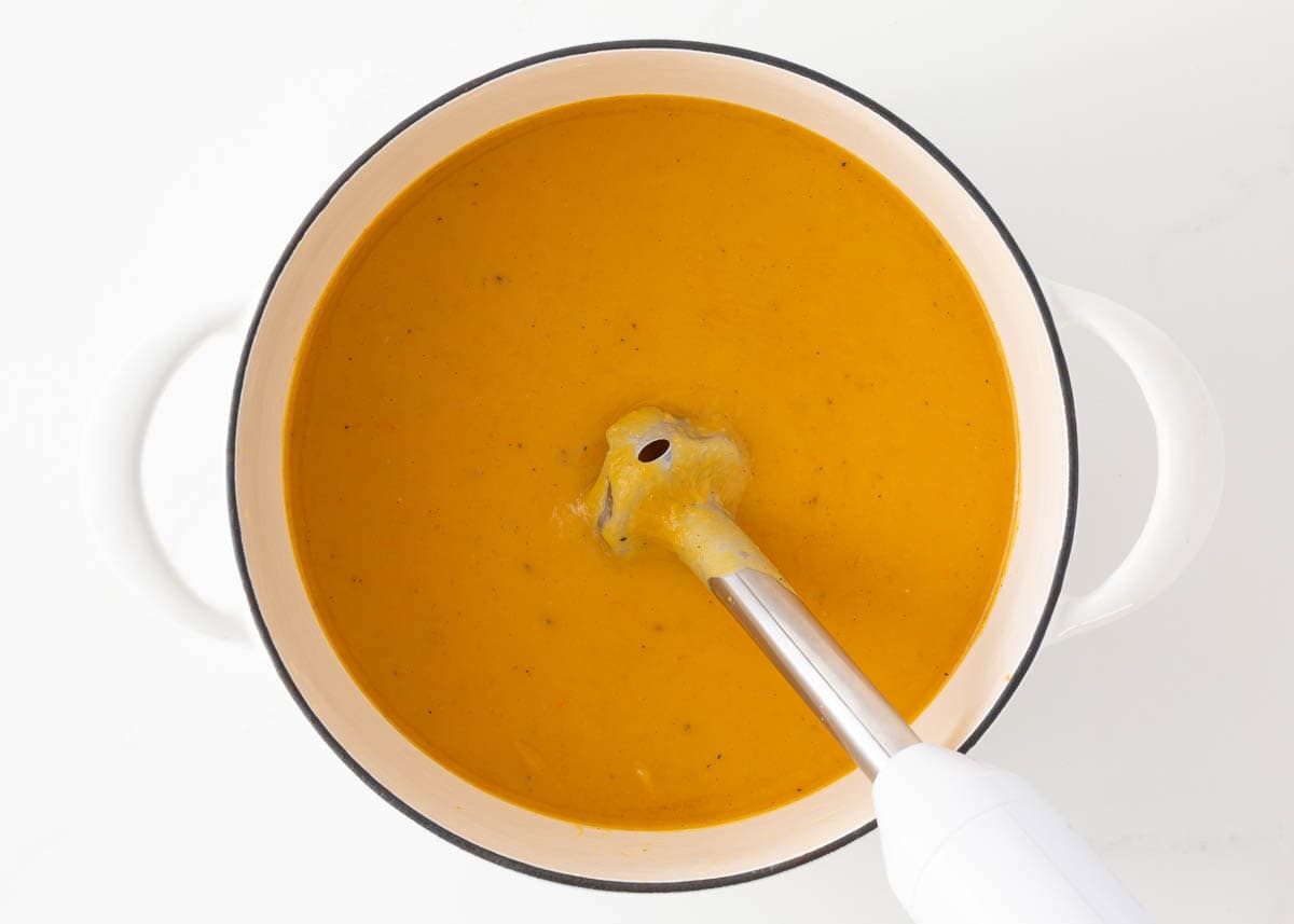 Using an immersion blender to puree butternut squash soup.