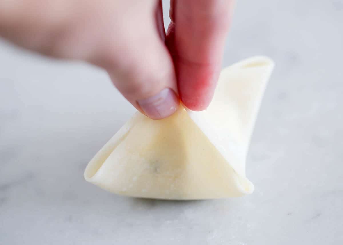 Showing how to fold a wonton wrapper with cream cheese filling. 