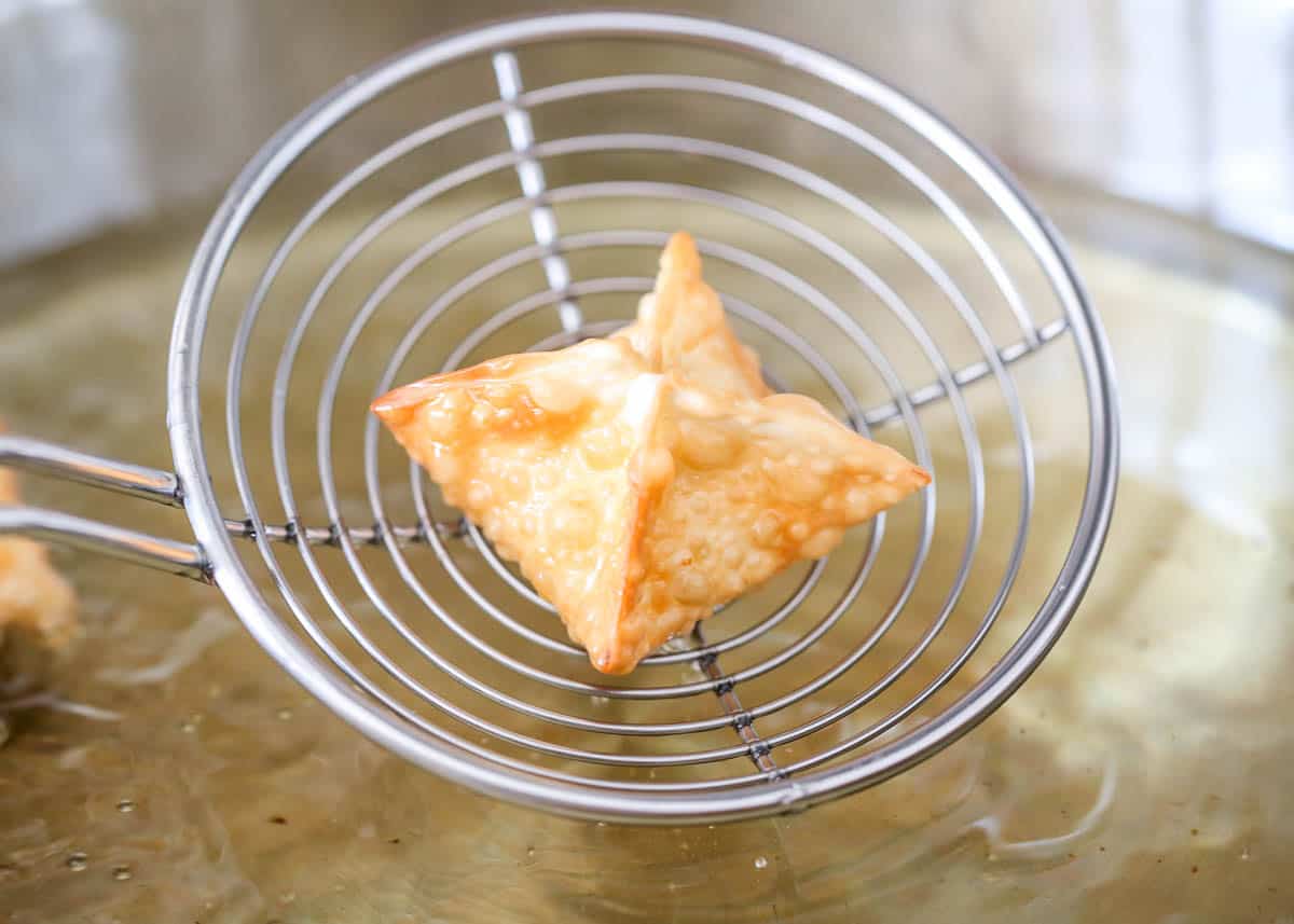 A fried cream cheese wonton in a scooper for deep frying.