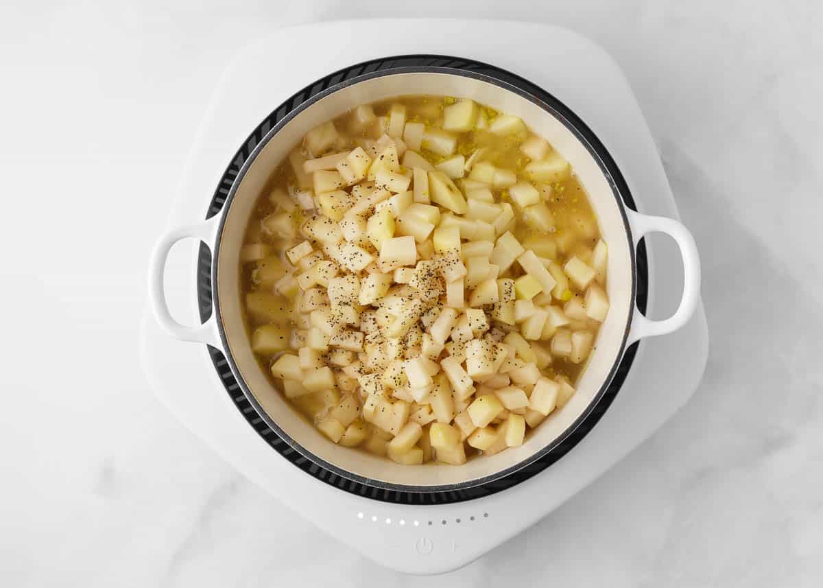 Adding diced potatoes to a pot of soup ingredients. 