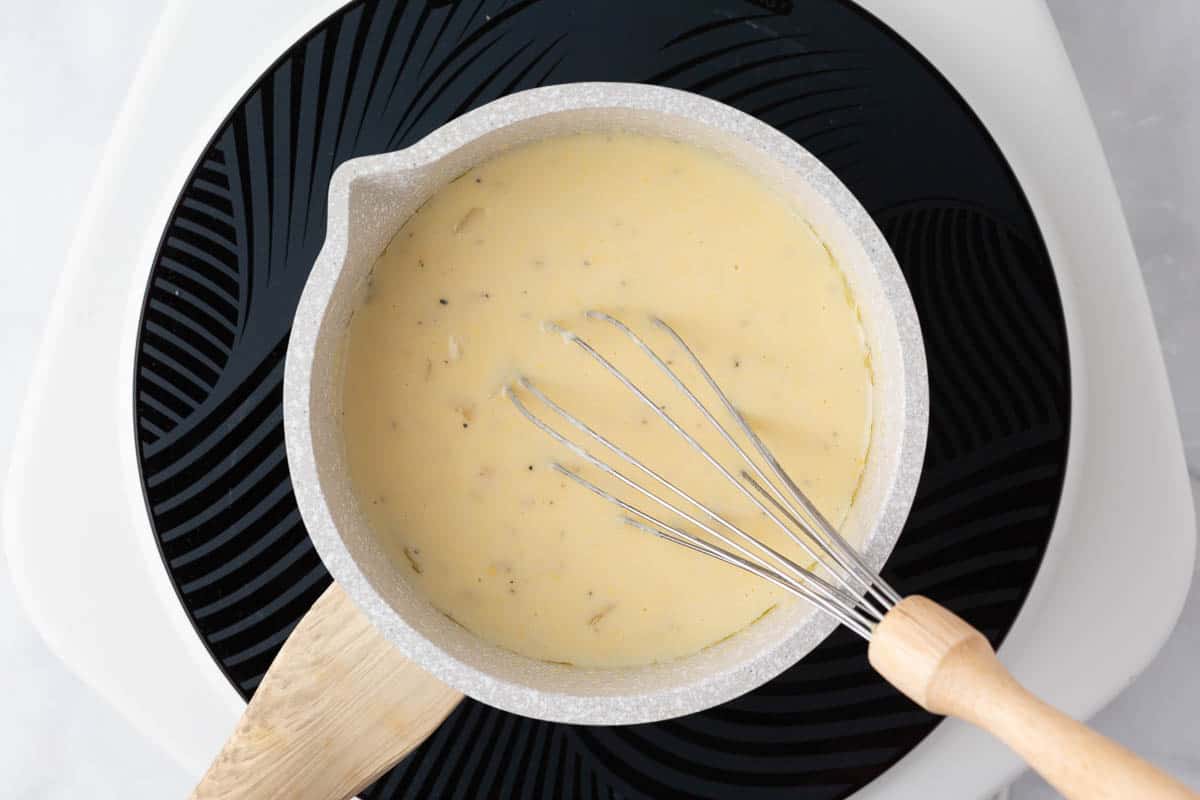 Making a cheese sauce in a pot with a whisk.