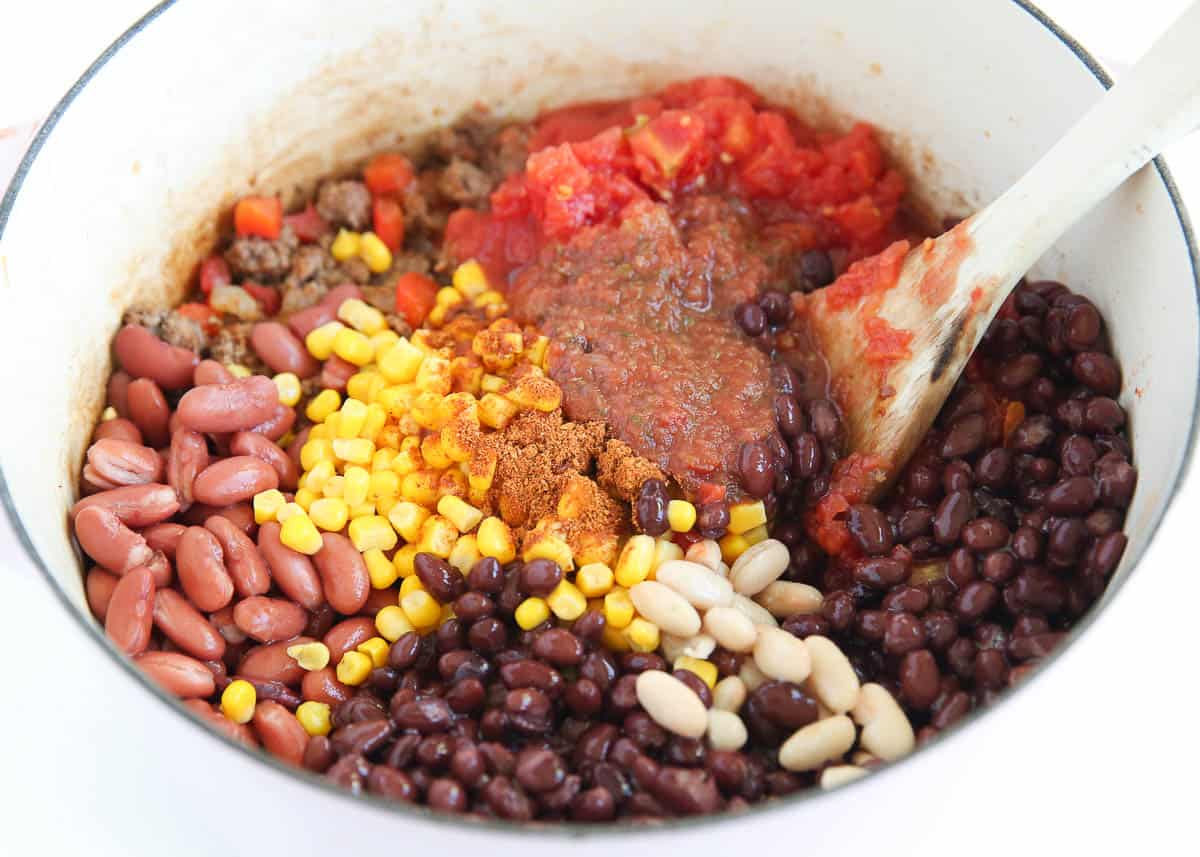 Adding beans, corn, seasonings and tomatoes to a pot of taco soup.