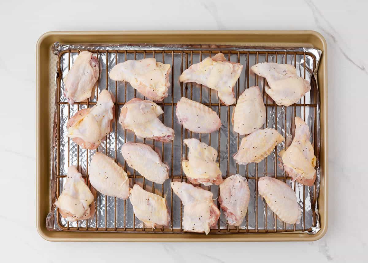 Seasoned and coated in baking powder chicken wings on wire rack set on baking sheet.