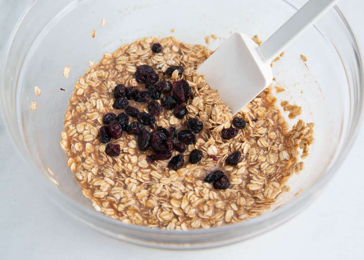 Oats, sugar, baking powder, salt, cinnamon and raisins stirred into liquid ingredients in a bowl.