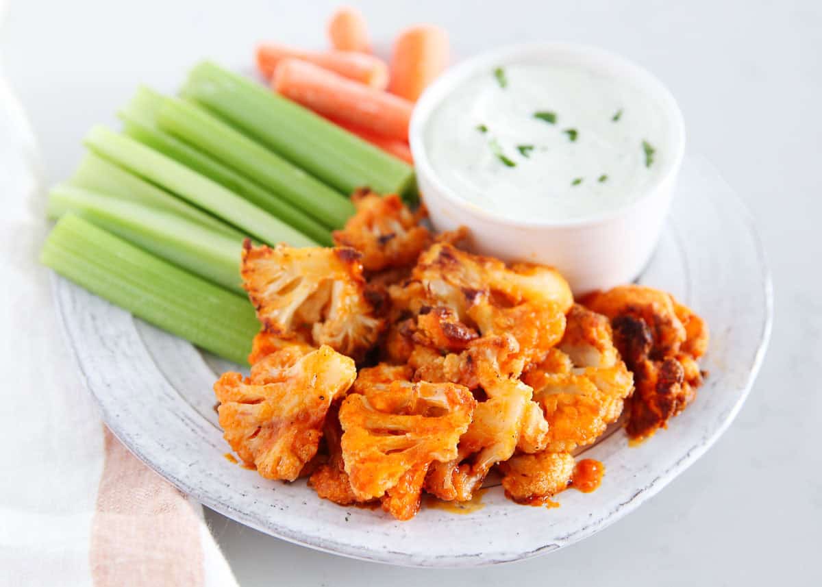 Buffalo cauliflower wings on a plate with celery and ranch dressing.