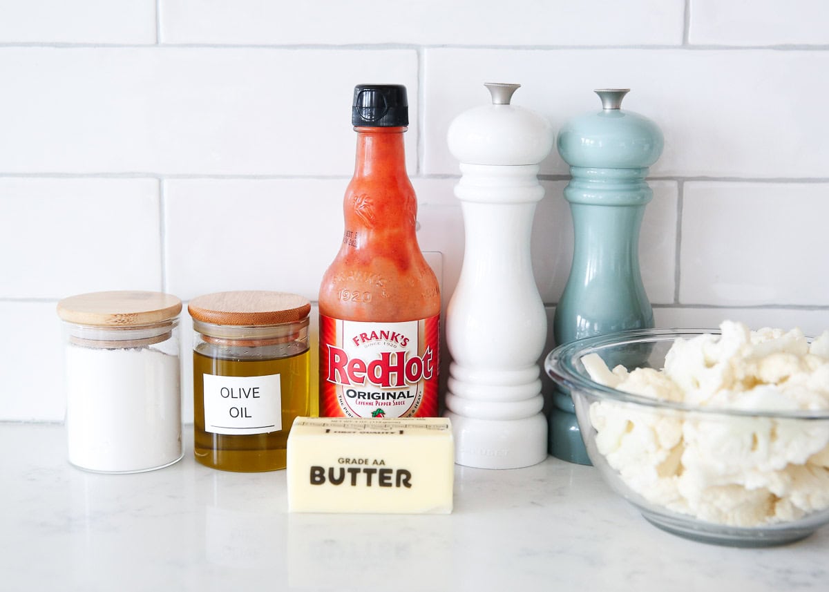 Butter, red hot sauce, cauliflower florets, flour and cornstarch on the counter.