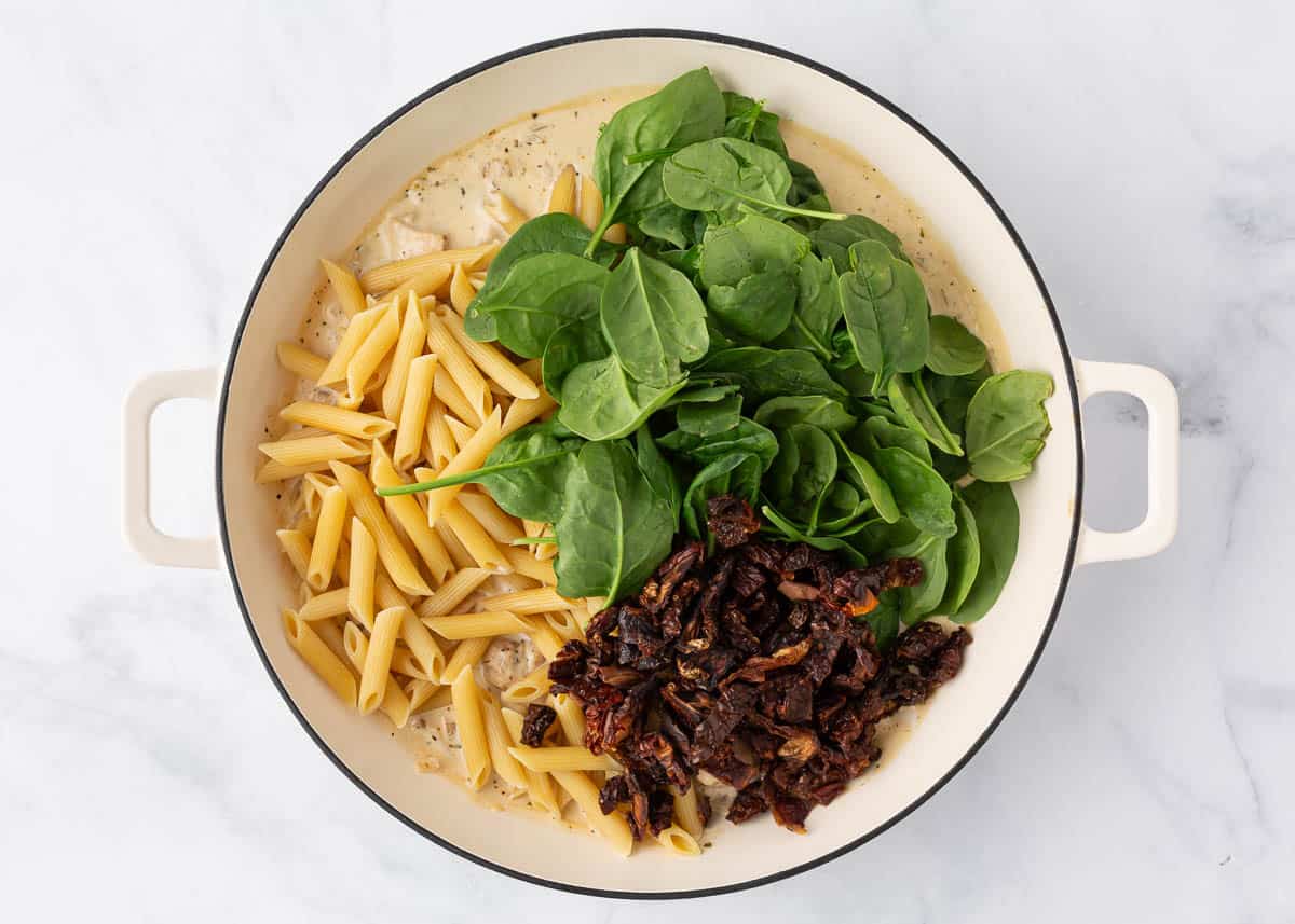 Pasta, spinach and sundried tomatoes in a skillet.