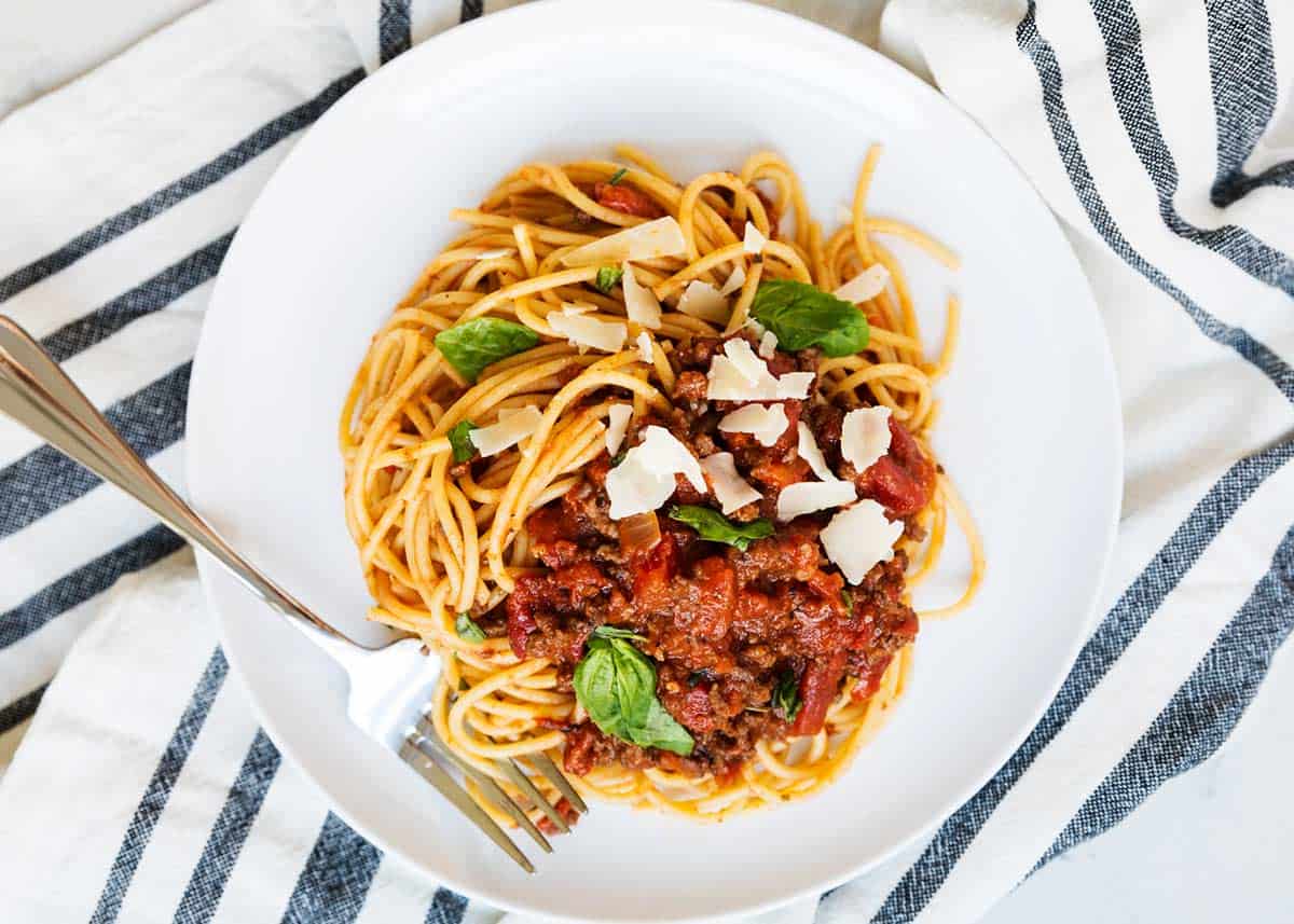 Spaghetti bolognese sauce on a white plate with pasta and garnish.