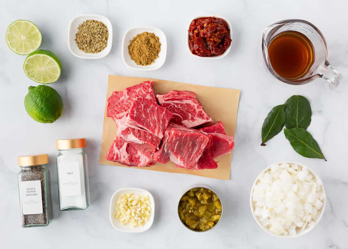 Beef chuck roast, onion, chipotle in adobo sauce, limes, garlic and seasonings on the counter.