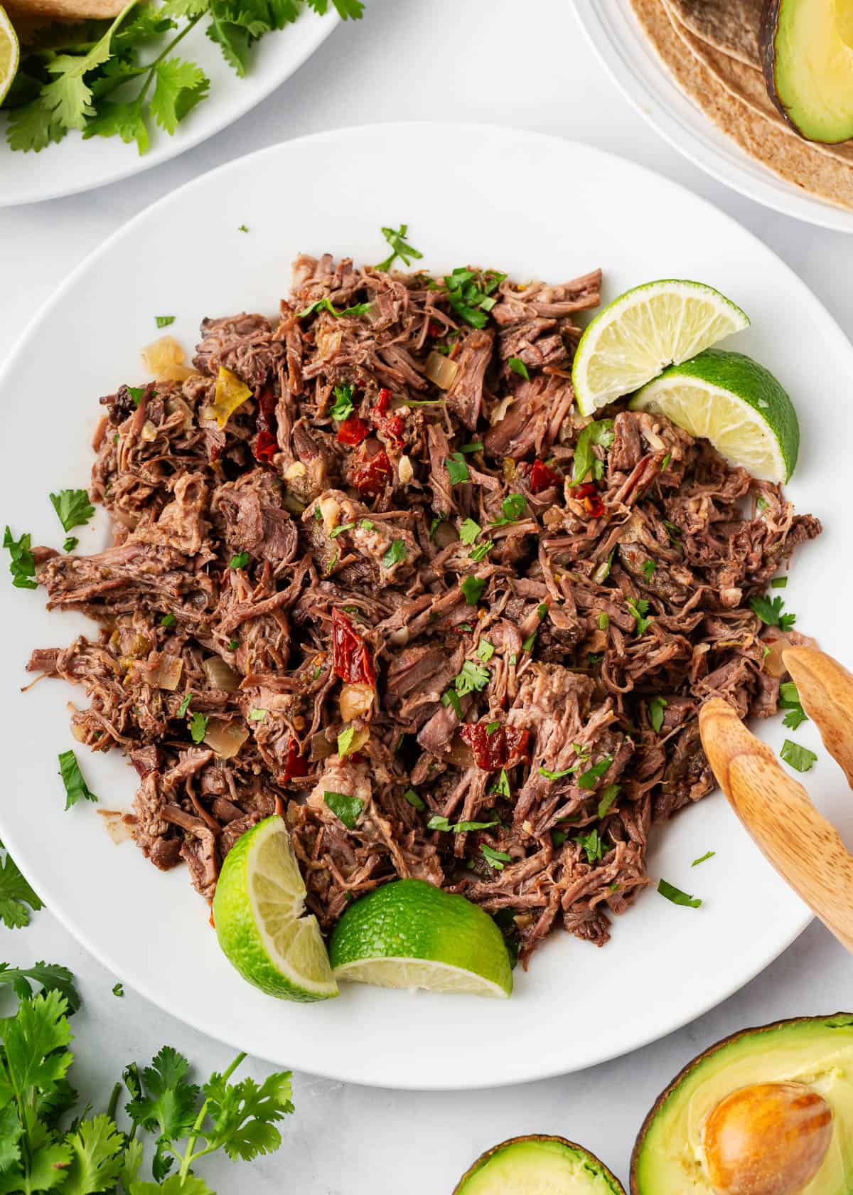 Barbacoa beef shredded on a plate with lime wedges.