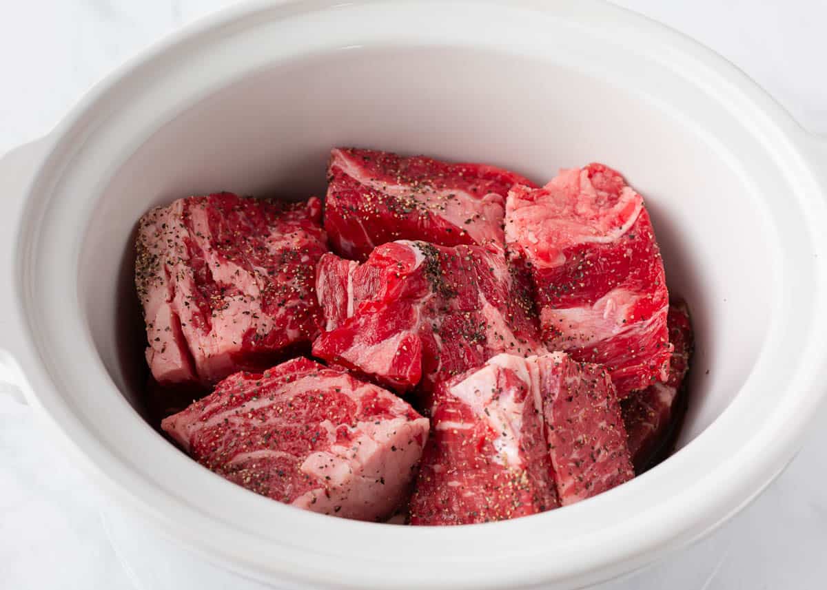 Beef roast cut into pieces, seasoned and in the bottom of a slow cooker. 