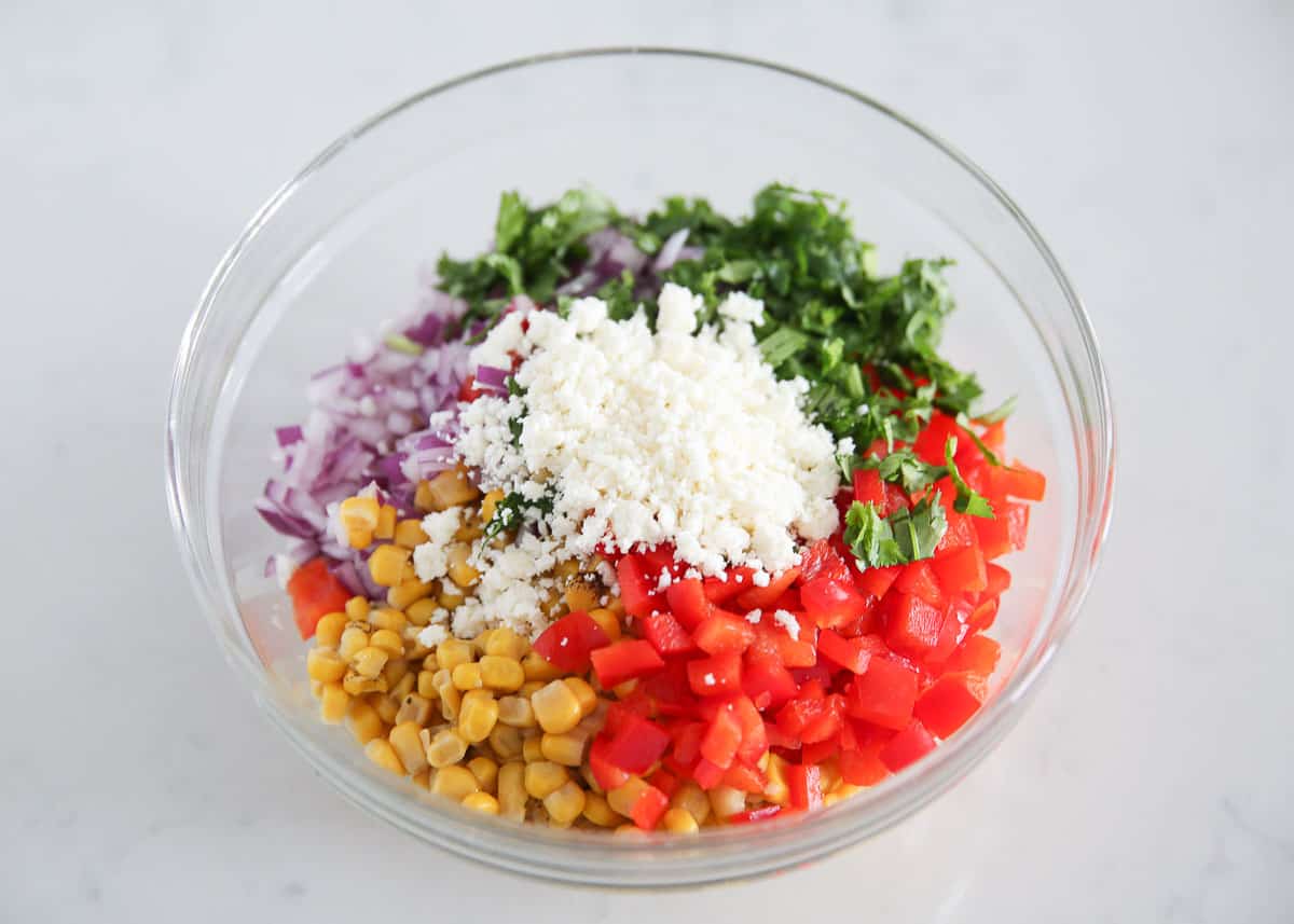 Corn, bell pepper, onion, cilantro, and cotija cheese together in a bowl.