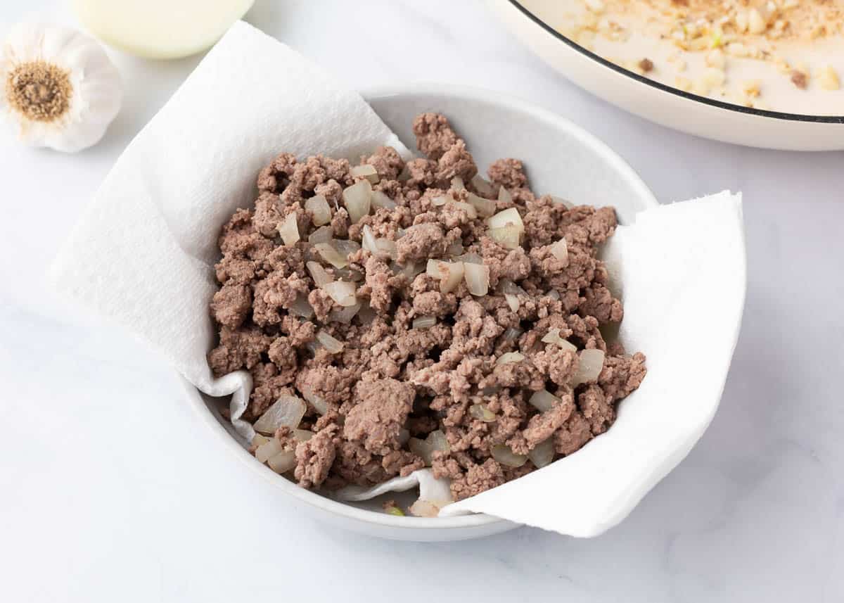 Ground beef and onion draining in paper towel lined bowl.