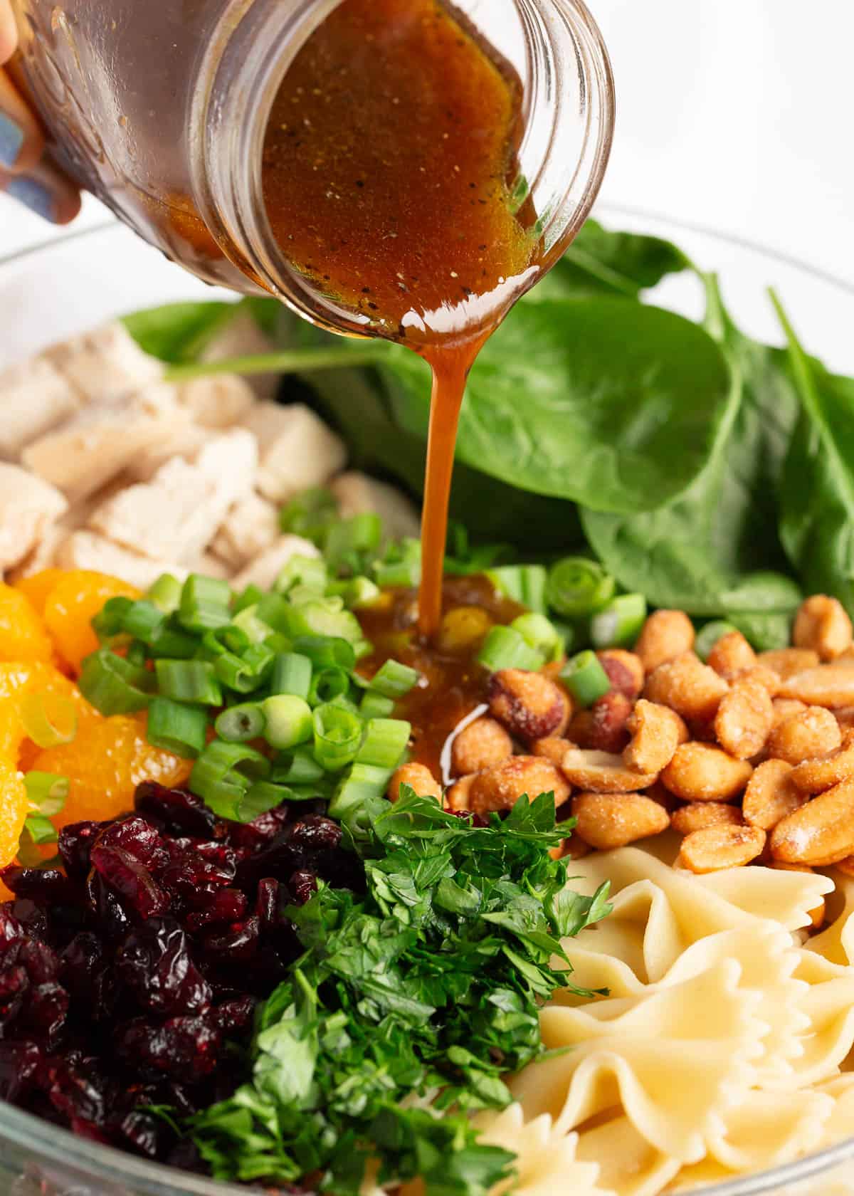 Pouring dressing on top of spinach pasta salad.